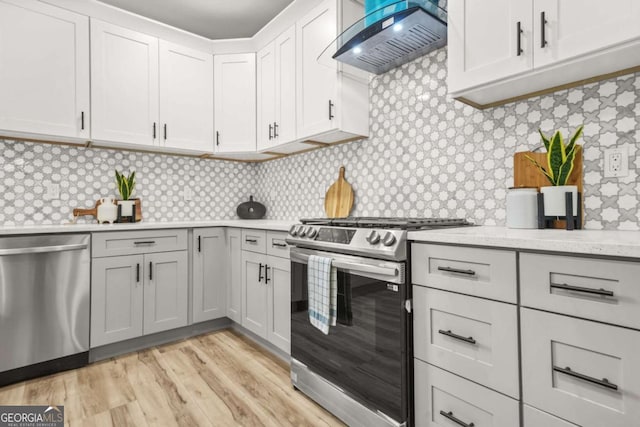 kitchen featuring wall chimney range hood, gray cabinets, light wood-style flooring, stainless steel appliances, and backsplash