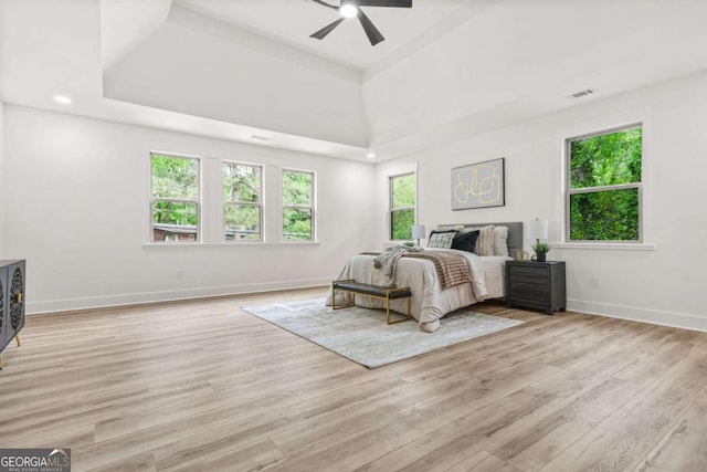 bedroom with visible vents, light wood-style floors, baseboards, and a tray ceiling