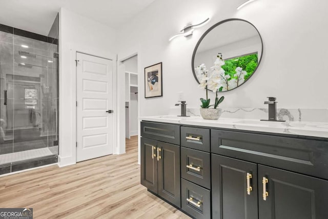full bathroom with double vanity, a shower stall, a sink, and wood finished floors