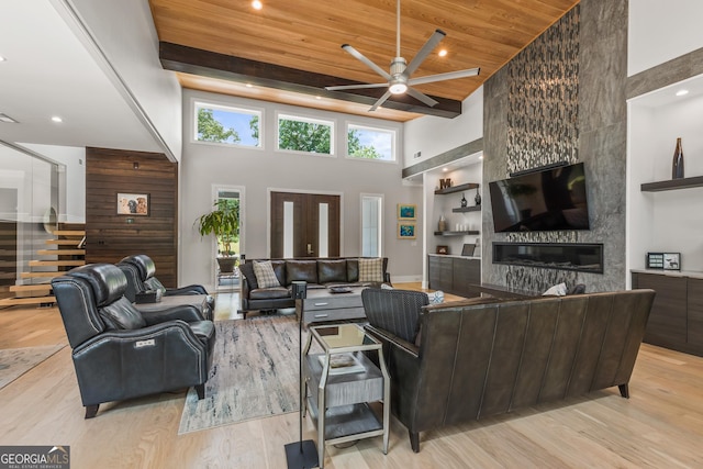living room with ceiling fan, a large fireplace, wood finished floors, a towering ceiling, and wood ceiling
