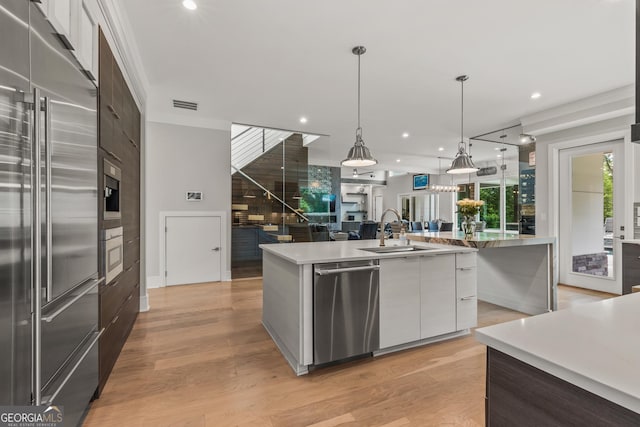 kitchen featuring appliances with stainless steel finishes, modern cabinets, a large island with sink, a sink, and white cabinetry