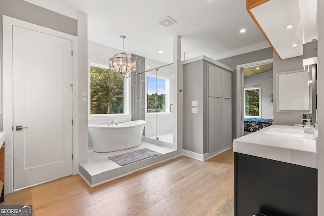 bathroom with a freestanding bath, an inviting chandelier, vanity, wood finished floors, and a stall shower