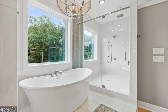 full bath featuring a notable chandelier, tile patterned flooring, baseboards, a soaking tub, and a stall shower