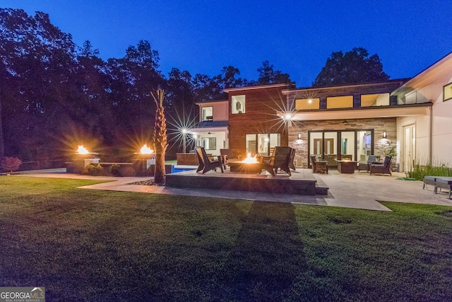 back of house at twilight with a lawn, an outdoor living space with a fire pit, and a patio