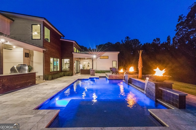 pool at night with a ceiling fan, a patio area, exterior kitchen, and an outdoor pool