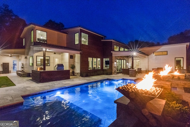 back of house at night with an outdoor living space with a fire pit, ceiling fan, a patio area, and an outdoor pool