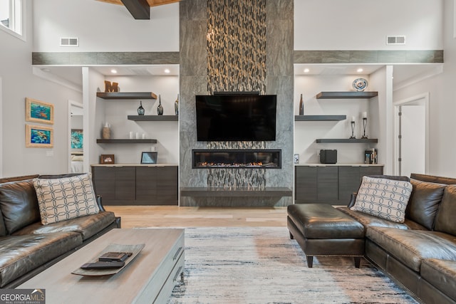living area featuring visible vents, a towering ceiling, wood finished floors, and a fireplace