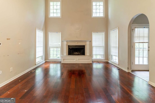 6416 Vicksburg Ct NW, Acworth, GA 30101 - unfurnished living room with a towering ceiling, hardwood / wood-style floors, a fireplace with raised hearth, arched walkways, and baseboards