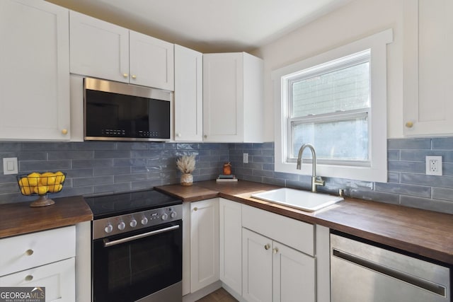 kitchen with a sink, stainless steel appliances, butcher block countertops, and white cabinetry