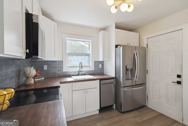 kitchen featuring appliances with stainless steel finishes, a sink, wood counters, white cabinetry, and decorative backsplash