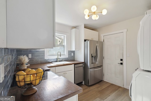 kitchen with stacked washer and dryer, appliances with stainless steel finishes, tasteful backsplash, a sink, and white cabinets