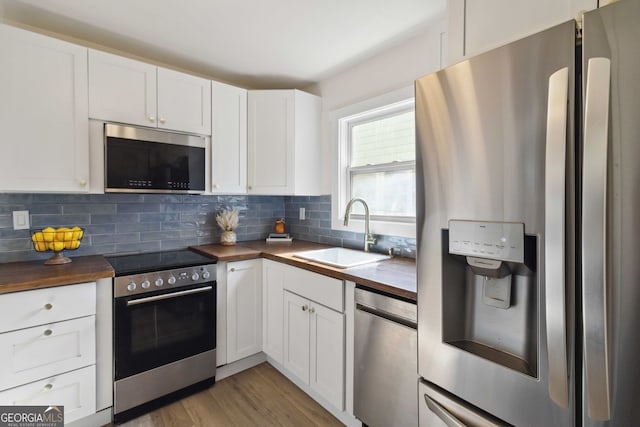 kitchen with decorative backsplash, appliances with stainless steel finishes, a sink, white cabinets, and wood counters