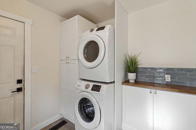 clothes washing area with stacked washing maching and dryer, baseboards, cabinet space, and wood finished floors