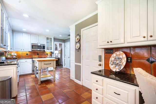 kitchen featuring crown molding, white cabinets, a sink, stainless steel microwave, and backsplash