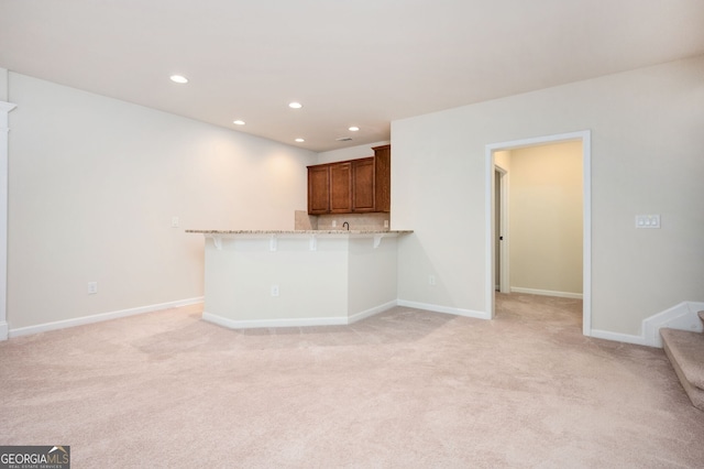 6732 Chimney Ridge Ct, Hoschton, GA 30548 - kitchen featuring recessed lighting, light colored carpet, a peninsula, brown cabinetry, and a breakfast bar