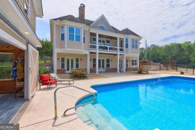 rear view of house with french doors, a chimney, a patio area, fence, and a balcony