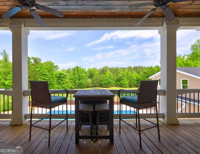 wooden terrace featuring a swimming pool, a ceiling fan, and a forest view