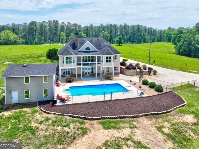 rear view of house with a balcony, a fenced backyard, a fenced in pool, a patio area, and a lawn