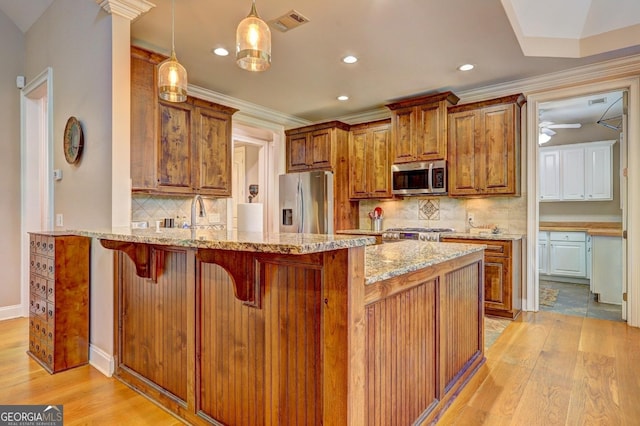 kitchen with appliances with stainless steel finishes, light stone countertops, brown cabinets, a peninsula, and light wood finished floors