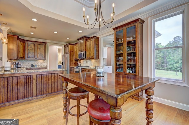 kitchen with appliances with stainless steel finishes, a chandelier, decorative backsplash, light wood-type flooring, and ornamental molding