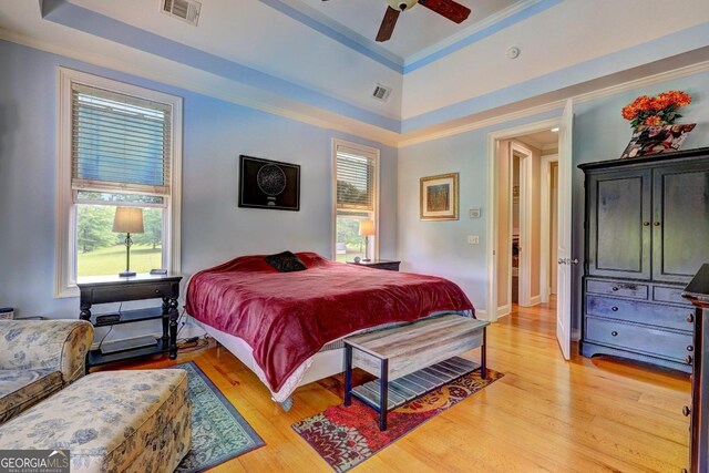 bedroom with visible vents, crown molding, a tray ceiling, and light wood-type flooring