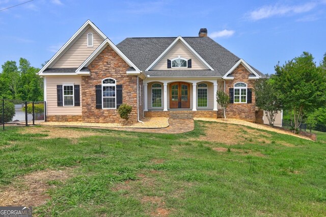 craftsman-style house with a chimney, a front yard, and stone siding