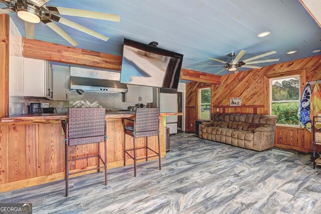 kitchen featuring ceiling fan, wood finished floors, a wealth of natural light, and wall chimney range hood