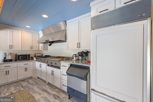 kitchen with white cabinets, wall chimney exhaust hood, recessed lighting, stainless steel microwave, and paneled fridge