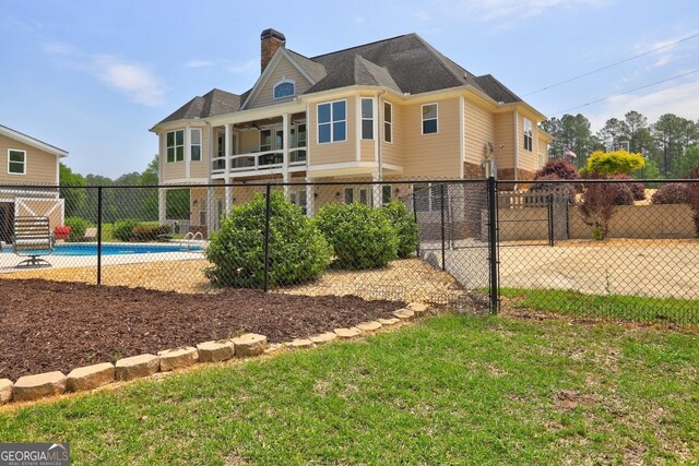 rear view of property with a lawn, fence, a chimney, and a fenced in pool