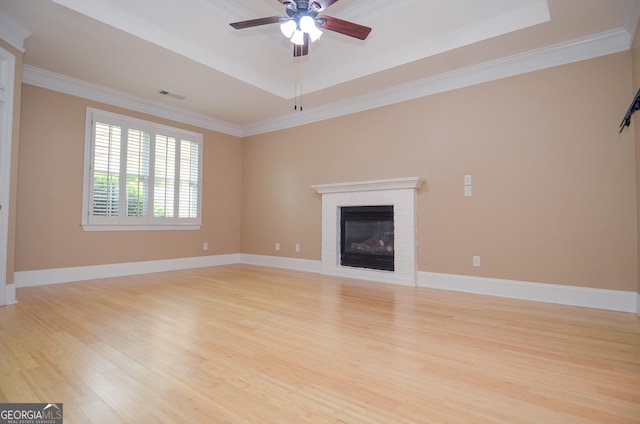 unfurnished living room featuring a raised ceiling, a ceiling fan, light wood-type flooring, visible vents, and ornamental molding