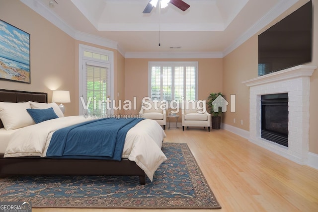 bedroom featuring ornamental molding, wood finished floors, a fireplace, a tray ceiling, and a ceiling fan