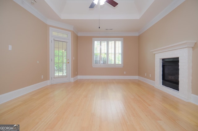 unfurnished living room featuring a brick fireplace, a ceiling fan, a tray ceiling, and light wood finished floors