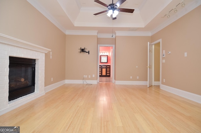 unfurnished living room with a brick fireplace, a tray ceiling, ceiling fan, and light wood-style flooring