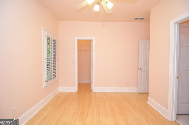 unfurnished bedroom with ceiling fan, light wood-style flooring, baseboards, a spacious closet, and visible vents