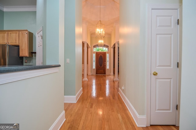 corridor featuring baseboards, ornamental molding, light wood-type flooring, and a notable chandelier