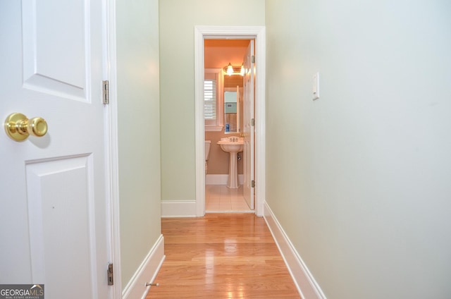 hallway featuring light wood-style floors, baseboards, and a sink