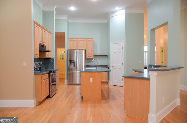 kitchen with light brown cabinetry, dark countertops, an island with sink, under cabinet range hood, and stainless steel appliances