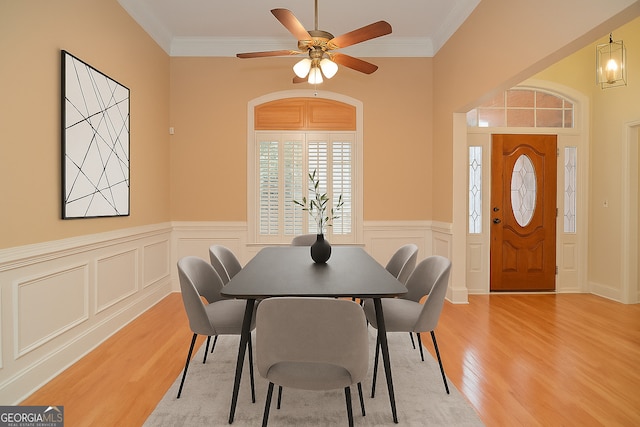 dining area featuring wainscoting, ornamental molding, a ceiling fan, and light wood-type flooring