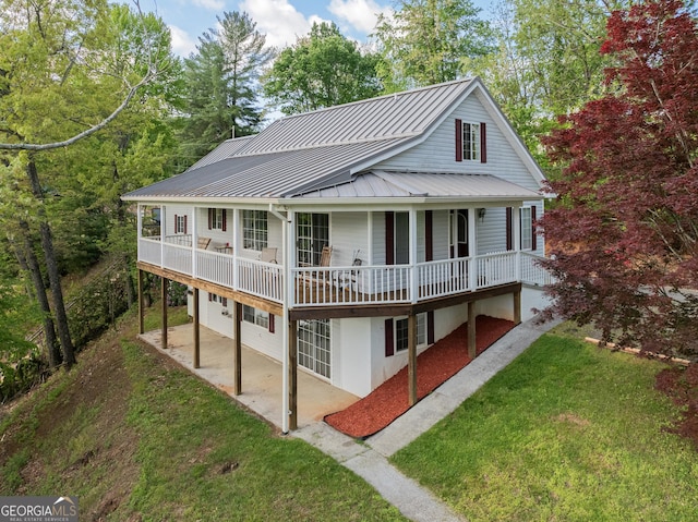 rear view of property with a standing seam roof, a lawn, a patio area, and metal roof