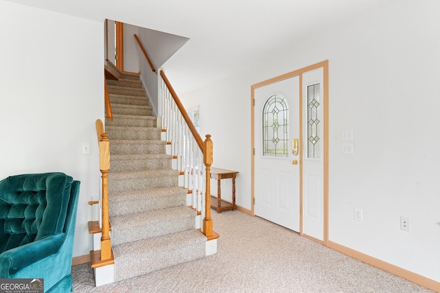carpeted foyer featuring baseboards and stairway