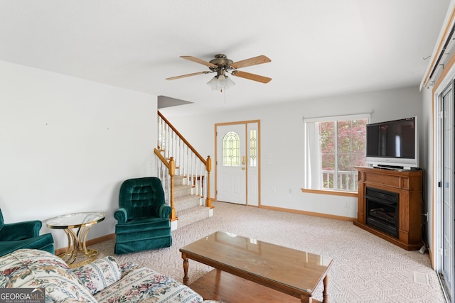 living area featuring a ceiling fan, baseboards, light colored carpet, and stairway