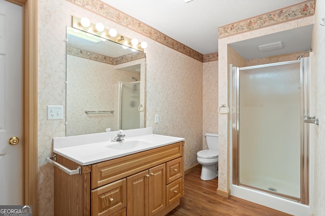 bathroom with a shower stall, wood finished floors, vanity, toilet, and wallpapered walls