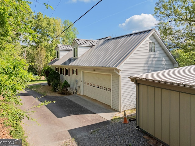 view of side of property featuring a garage, aphalt driveway, and metal roof