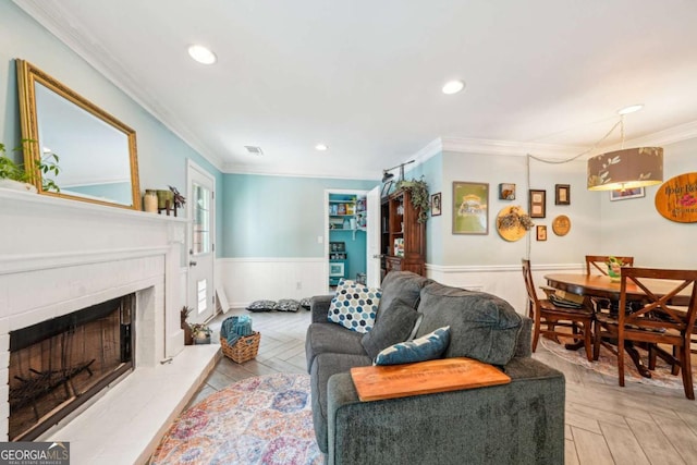 living room with a wainscoted wall, ornamental molding, a fireplace with raised hearth, and recessed lighting