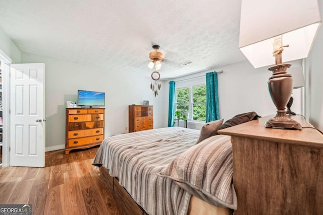 bedroom with a textured ceiling, baseboards, wood finished floors, a skylight, and visible vents