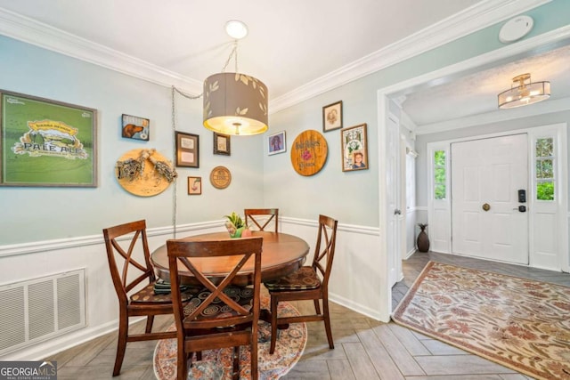 dining room featuring crown molding, visible vents, and a wainscoted wall