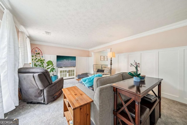 living area featuring a textured ceiling, crown molding, a wainscoted wall, carpet, and a decorative wall