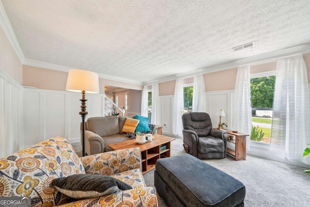 carpeted living room featuring crown molding, wainscoting, a decorative wall, and visible vents