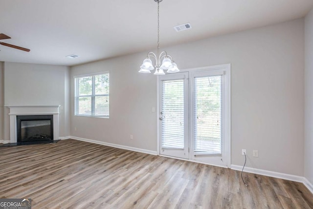 1003 Eldon Ln, Fairburn, GA 30213 - unfurnished living room featuring ceiling fan with notable chandelier, wood finished floors, visible vents, baseboards, and a glass covered fireplace