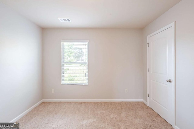 spare room featuring baseboards, light colored carpet, and visible vents